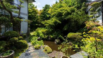 Un jardín japonés tradicional con un estanque de carpas koi, senderos de piedra y diversas plantas.