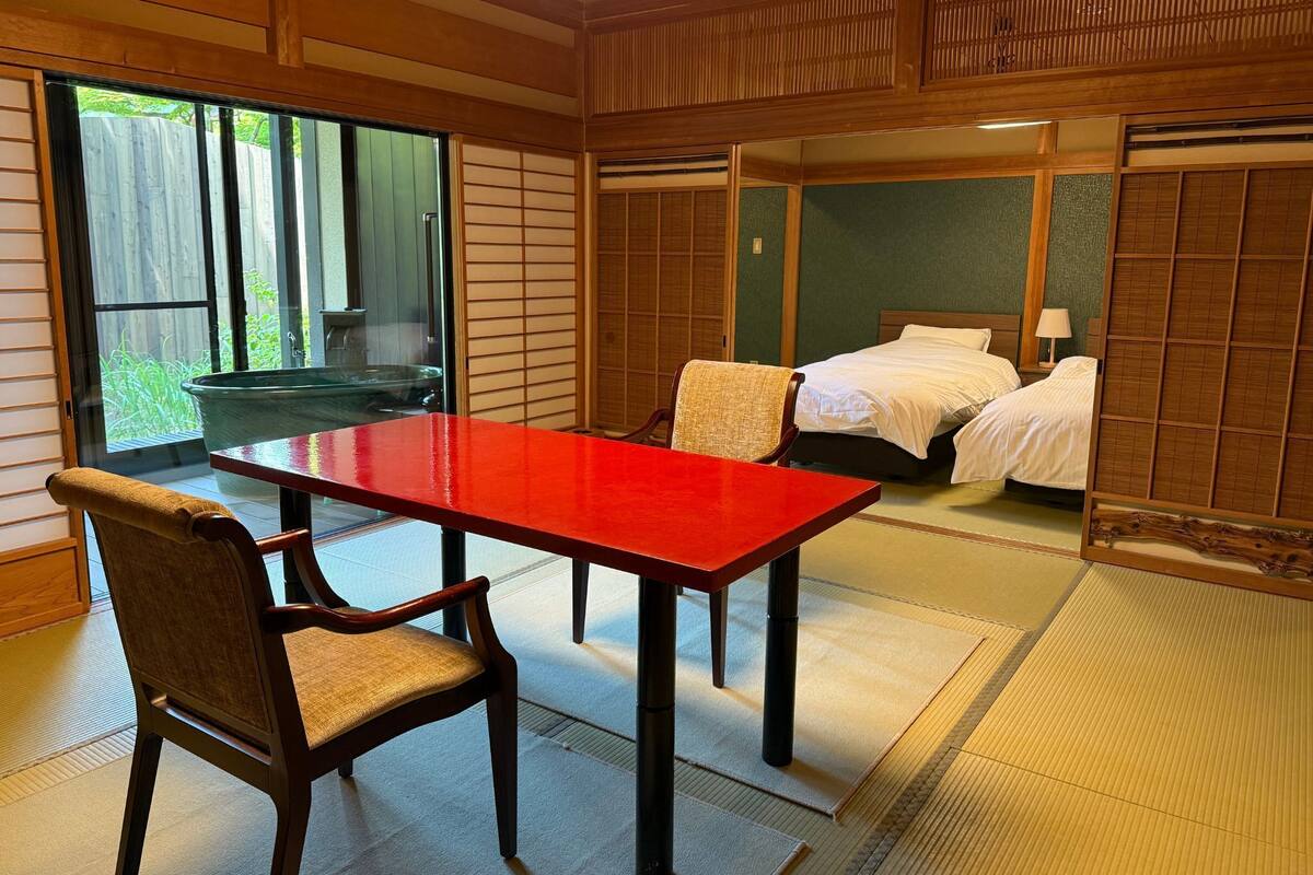A traditional Japanese room with tatami flooring, a wooden table, and a bed with a futon.