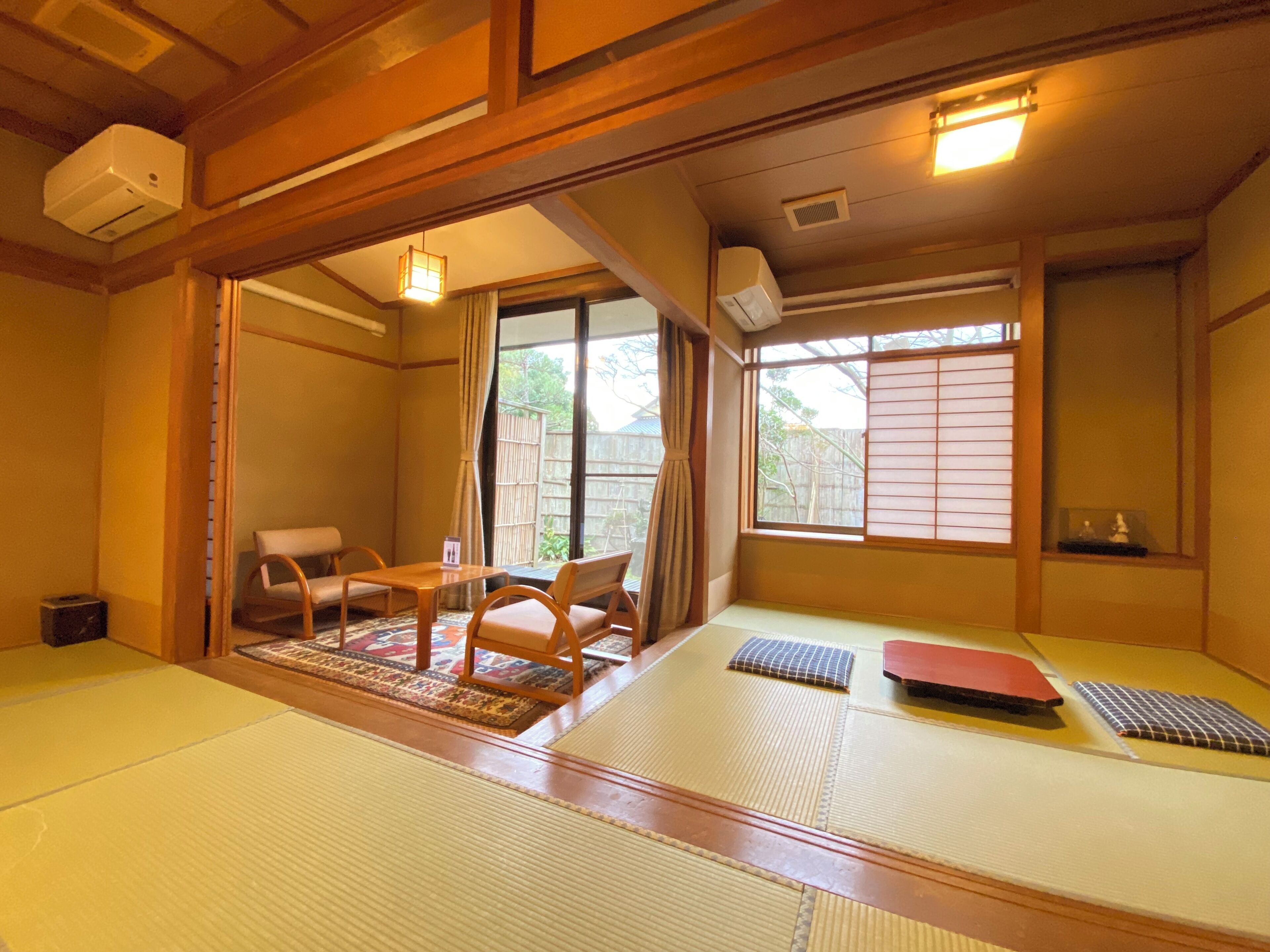 Um quarto japonês tradicional com tatame, uma mesa baixa com cadeiras e portas deslizantes.