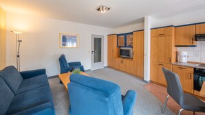 A compact living space with a kitchenette, a dining area with blue furniture, and a small TV. - Haus Strandruh (Binz)