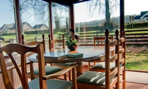 Ein Essbereich mit einem runden Tisch, Holzstühlen mit grünen Kissen und Blick auf eine Wohngegend durch große Fenster.