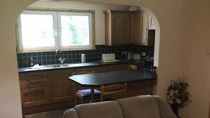 Een woonkamer met een bank, een eettafel en een keuken met houten kasten en een raam.