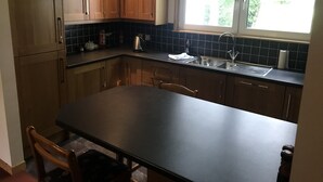 Een keuken met houten kastjes, een zwart aanrecht, een gootsteen en een raam met uitzicht op groen.
