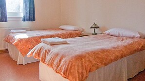 Een kamer met twee eenpersoonsbedden, elk met een witte dekbedovertrek en oranje beddengoed. Daartussen bevindt zich een nachtkastje met een lamp.