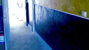 Ein Flur mit gelb-schwarzer Wand, einer Tür zu einem anderen Raum und einem kleinen Regal mit einigen Gegenständen.