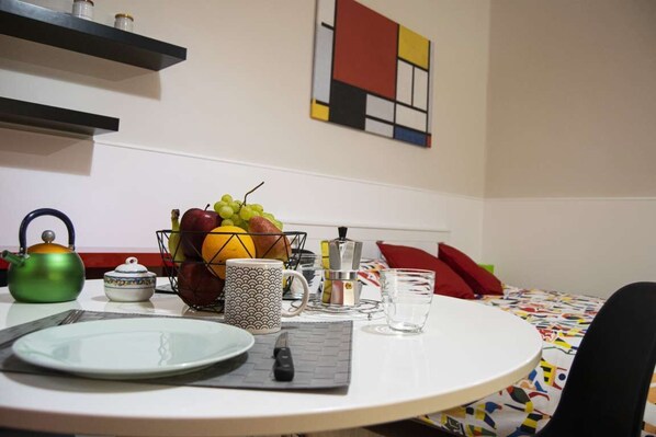 A dining area with a round table, a fruit basket, a kettle, and a vase.