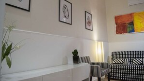Ein modernes Wohnzimmer mit einem weißen Konsolentisch, zwei gerahmten Kunstwerken, einem gemusterten Sofa und einem großen abstrakten Gemälde.