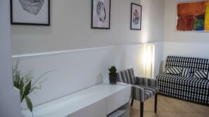 Ein modernes Wohnzimmer mit einem weißen Sofa, gestreiften Sesseln und einer Bank. An den Wänden hängen gerahmte Kunstwerke, und auf der Bank steht ein Topf mit einer Pflanze.