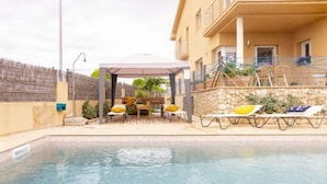 A swimming pool with lounge chairs and a covered seating area.