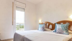 A bedroom with a bed, two pillows, a nightstand, a window, and a view of greenery outside.