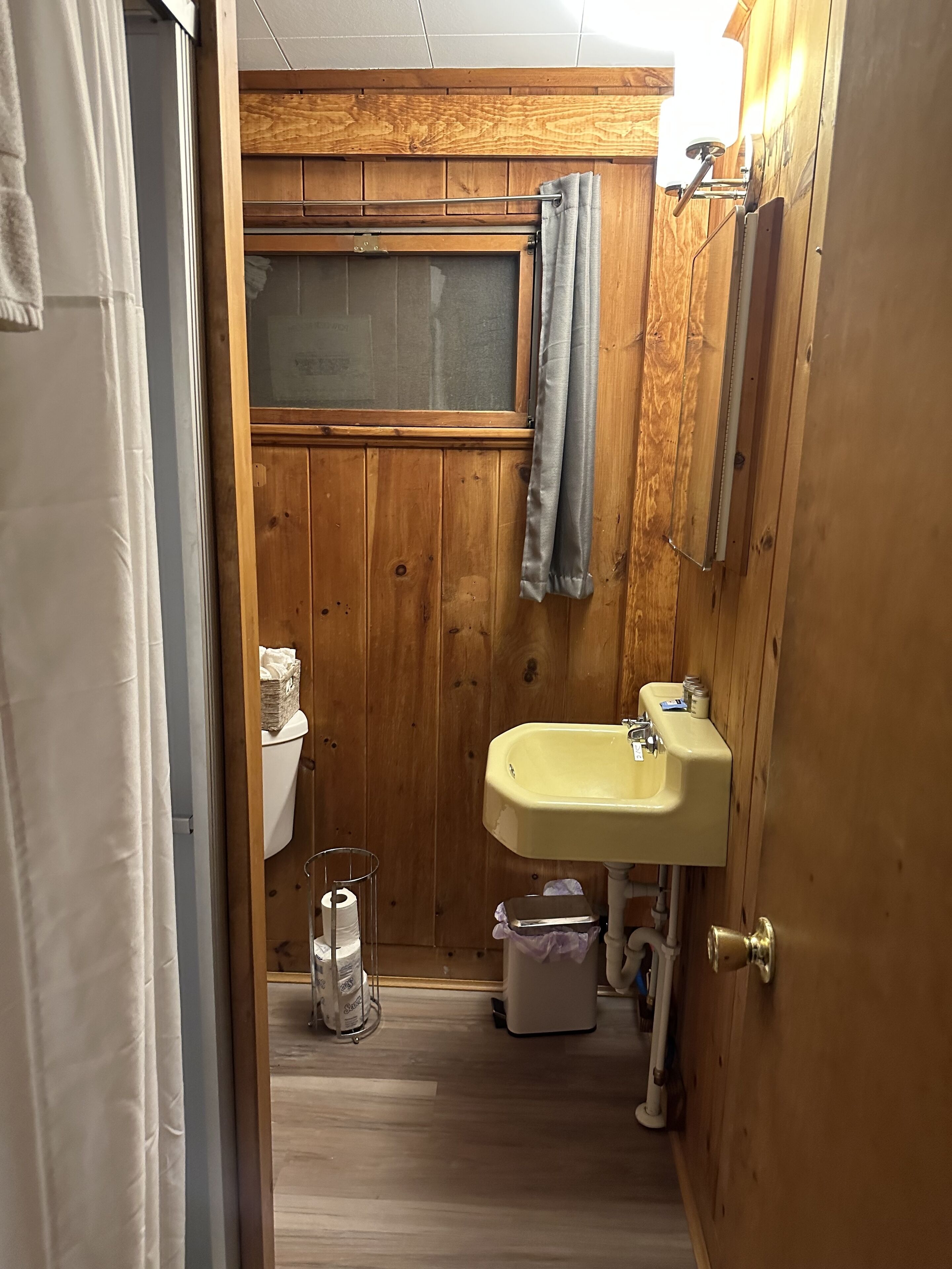 Un baño pequeño con paneles de madera, un inodoro, un lavabo y una ventana.