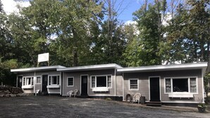 A row of two-story mobile homes with a gravel driveway and trees in the background.
