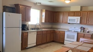 A kitchen with wooden cabinets, a refrigerator, a microwave, a stove, and a dining table. - “THE SALTY OLIVE"  SHORT WALK TO THE BEACH, FUR BABIES WELCOMED (Bolivar Peninsula)