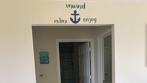 A hallway with a sign reading "unwind relax enjoy" and another sign saying "Memories made at the beach last a lifetime." - “THE SALTY OLIVE"  SHORT WALK TO THE BEACH, FUR BABIES WELCOMED (Bolivar Peninsula)