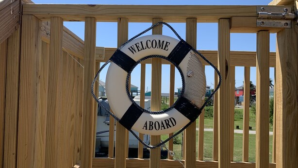 A wooden deck with a lifebuoy sign reading "WELCOME ABOARD" and a metal gate. - “THE SALTY OLIVE"  SHORT WALK TO THE BEACH, FUR BABIES WELCOMED (Bolivar Peninsula)