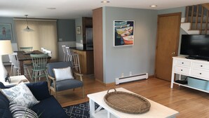 Una sala de estar con un sofá, una mesa de centro, un mueble para televisor y una zona de comedor con sillas y una mesa.