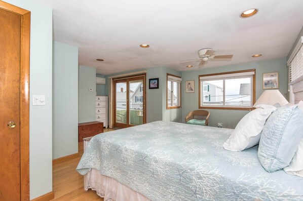 A bedroom with a bed, a ceiling fan, a window, and a door.