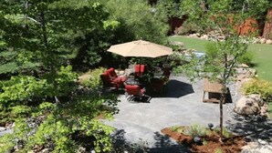 An outdoor patio with a table and chairs, surrounded by lush greenery and a small rock garden.