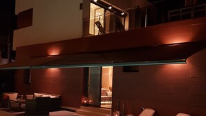 Un área de piscina moderna al aire libre con sillones de descanso y una escalera que lleva a un balcón en un segundo piso.