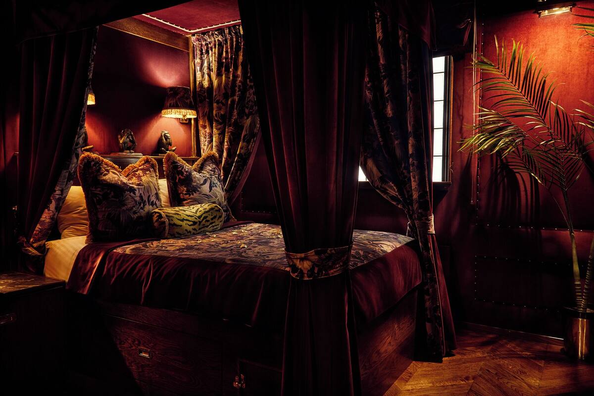 A dimly lit room with a large bed, a nightstand, a lamp, and a potted plant.