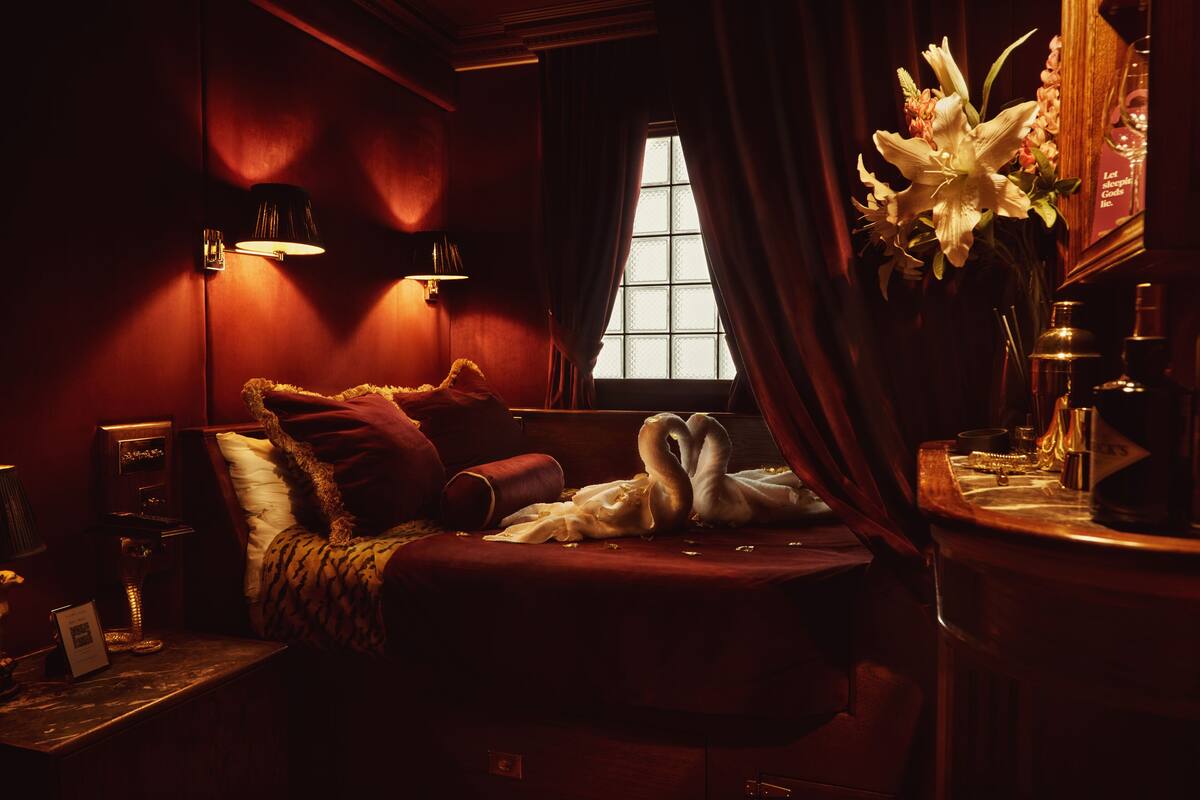 A dimly lit room with a bed, a nightstand, a mirror, and a window with curtains.