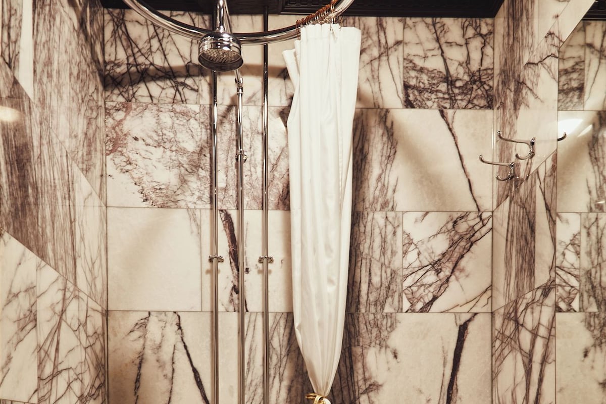 A bathroom with marble walls, a shower with a curtain, and a sink.