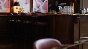 Uma área de bar com painéis de madeira, um balcão com banquetas e uma parede decorativa com estampas de flamingos.