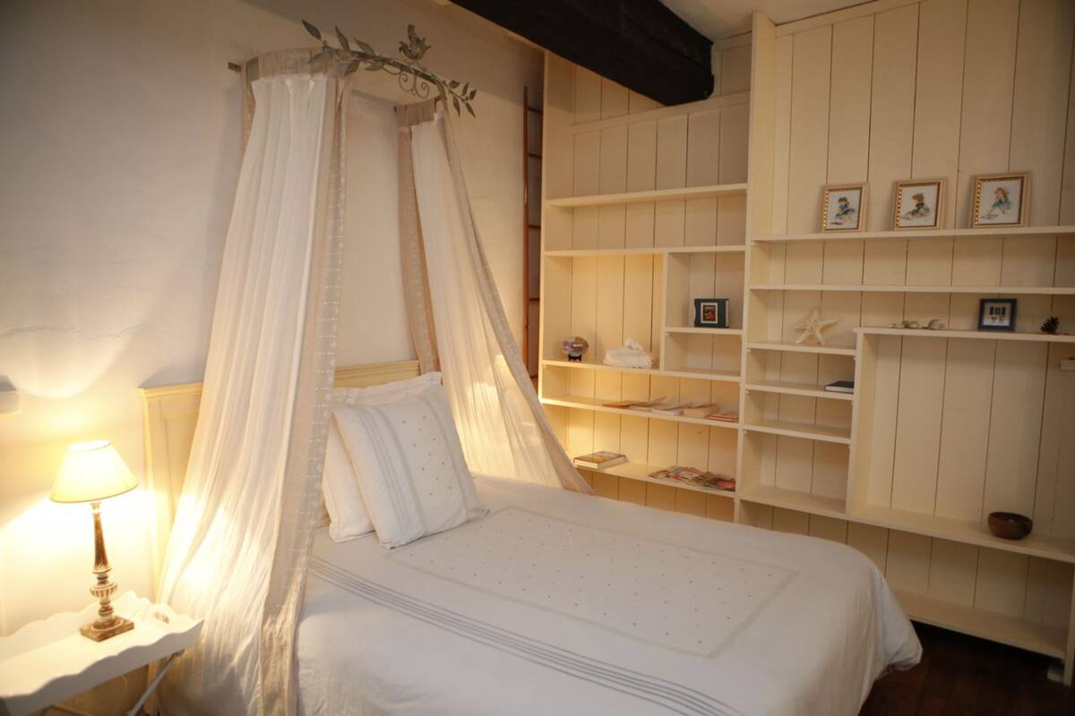 A bedroom with a canopy bed, bedside tables, and built-in shelving with framed pictures.