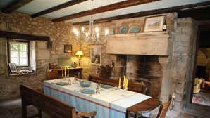 A stone-walled dining room with a long table set for four, a chandelier, and a fireplace. - Le Manoir Du Poul Coeur de Bretagne B&B (Mellionnec)