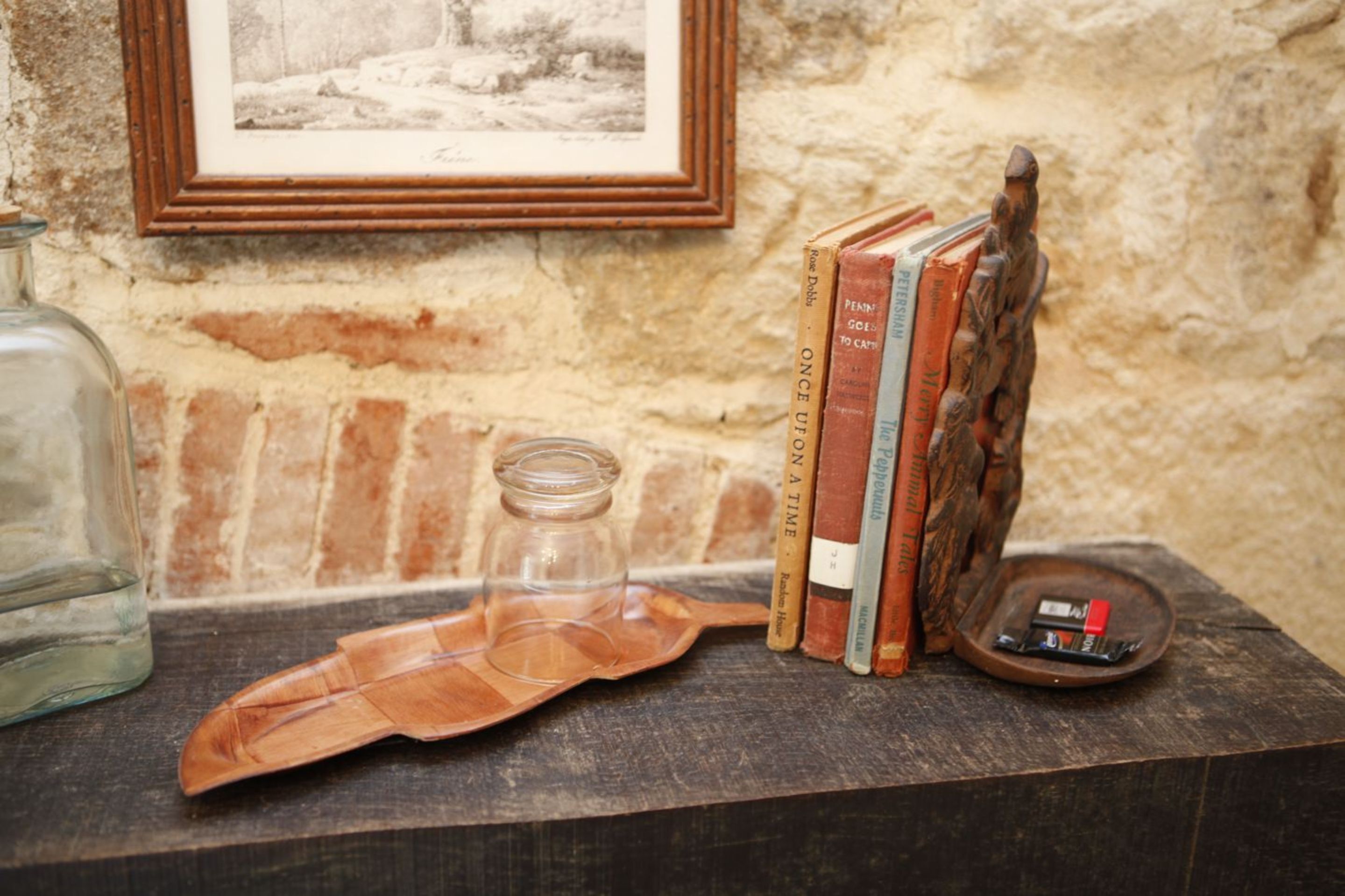 A wooden shelf with books, a glass jar, and a small figurine.