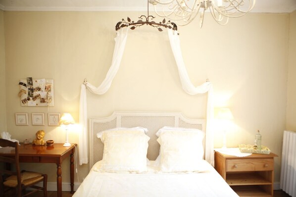 Un dormitorio con cama de dosel, lámparas de noche, una mesita de noche de madera y una pared decorada con cuadros.