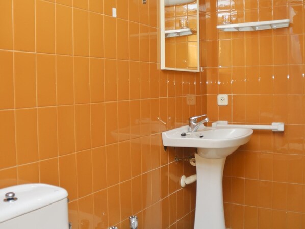 Une salle de bain avec des carreaux orange, un lavabo blanc, un miroir et des toilettes.