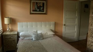 Un dormitorio con cama, mesita de noche, lámpara, puerta y un cuadro en la pared.