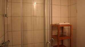Une douche avec une porte en verre, une étagère en bois où sont posées des serviettes et une pomme de douche en métal.