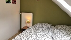 Une chambre avec un plafond en pente, un lit avec une literie à motifs, une lampe de chevet et deux tableaux encadrés accrochés au mur.