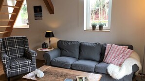Un salon avec un canapé, un fauteuil à motifs, une table basse en bois et une fenêtre agrémentée de plantes en pot.