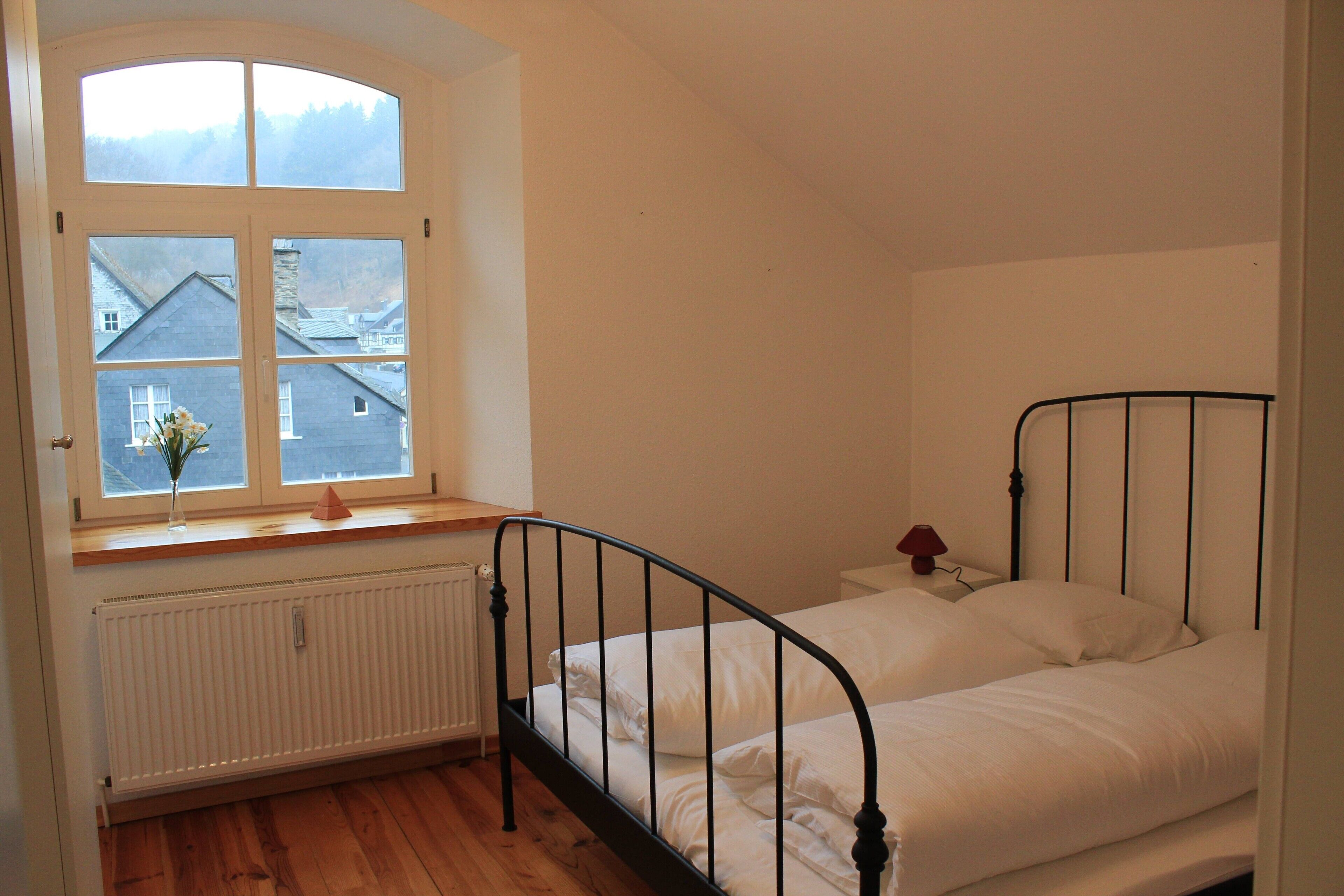 A bedroom with a single bed, a window with a view of houses, and a radiator.