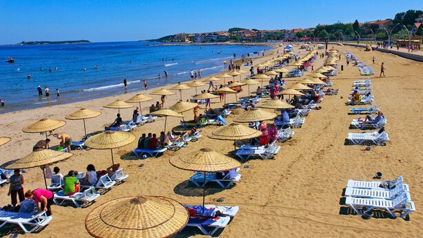 A beach with rows of sun loungers and thatched umbrellas, people sunbathing, and a clear blue sea. - Engin Otel (Kandira)