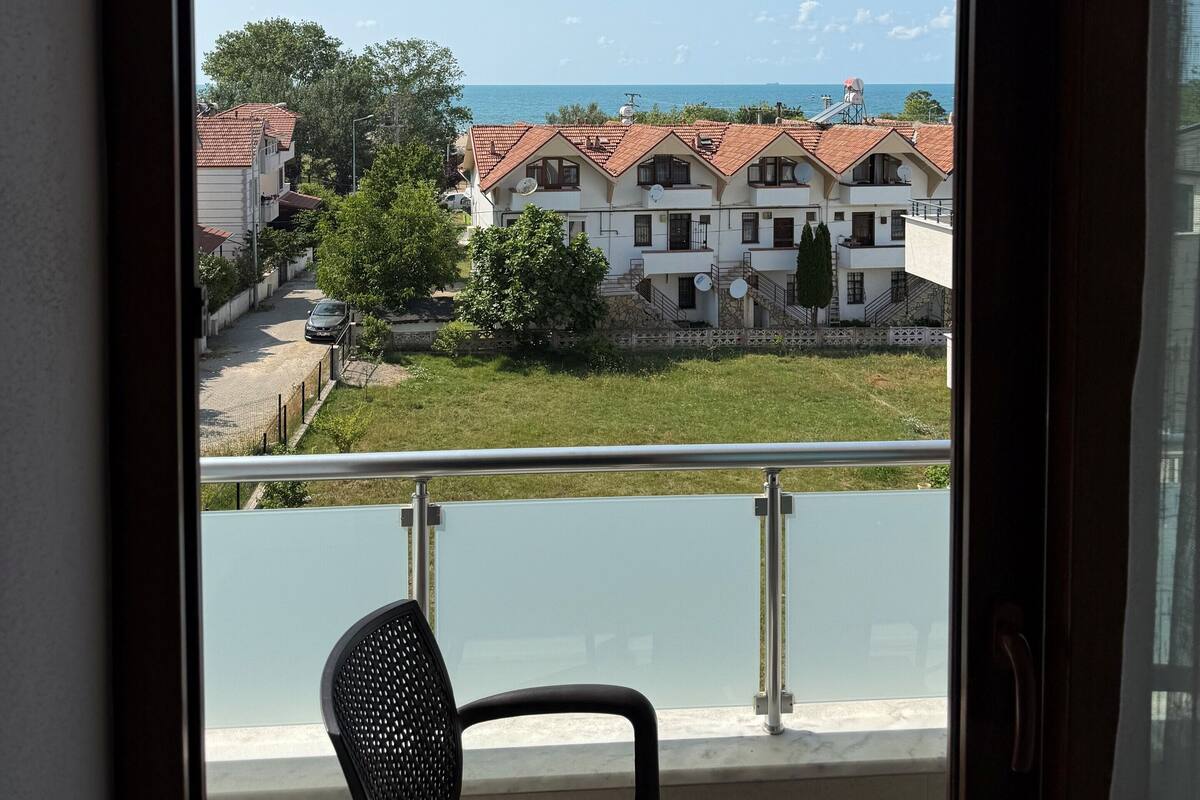 Ein Balkon mit Stuhl, Tisch und Blick auf ein Wohngebiet mit Häusern und einem Gewässer.