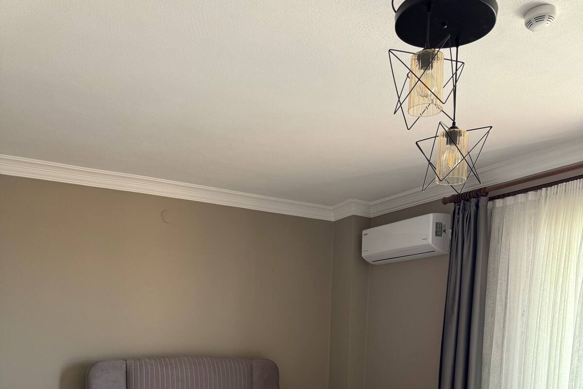 Ein ordentlich bezogenes Bett mit weißen Leinen, ein Nachttisch mit Lampe und ein Fenster mit Vorhängen.