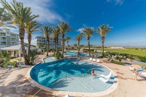 A resort pool area with palm trees, lounge chairs, and a clear blue sky.