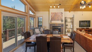 Una habitación amplia con una gran mesa de comedor, asientos cómodos, una chimenea y ventanas grandes que ofrecen vistas al exterior.