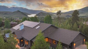 Una casa grande y moderna con terraza, paneles solares y vistas a montañas y un lago.