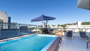 Une piscine sur le toit offrant une vue sur le paysage urbain, un espace salon couvert et un barbecue.