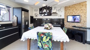 Une cuisine moderne avec un coin repas, comprenant un réfrigérateur, un téléviseur fixé à un mur en bois et une table avec des chaises.