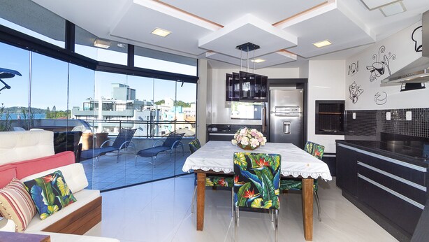 Une cuisine moderne équipée d’un réfrigérateur, d’une cuisinière et d’un plan de travail noir. On y trouve également un coin repas avec une table et des chaises, ainsi qu’un balcon agrémenté d’un canapé et de fauteuils.