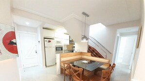Une cuisine moderne avec des armoires blanches, un four encastré et un four à micro-ondes. On y trouve également un coin repas avec une table en verre et des chaises en bois.