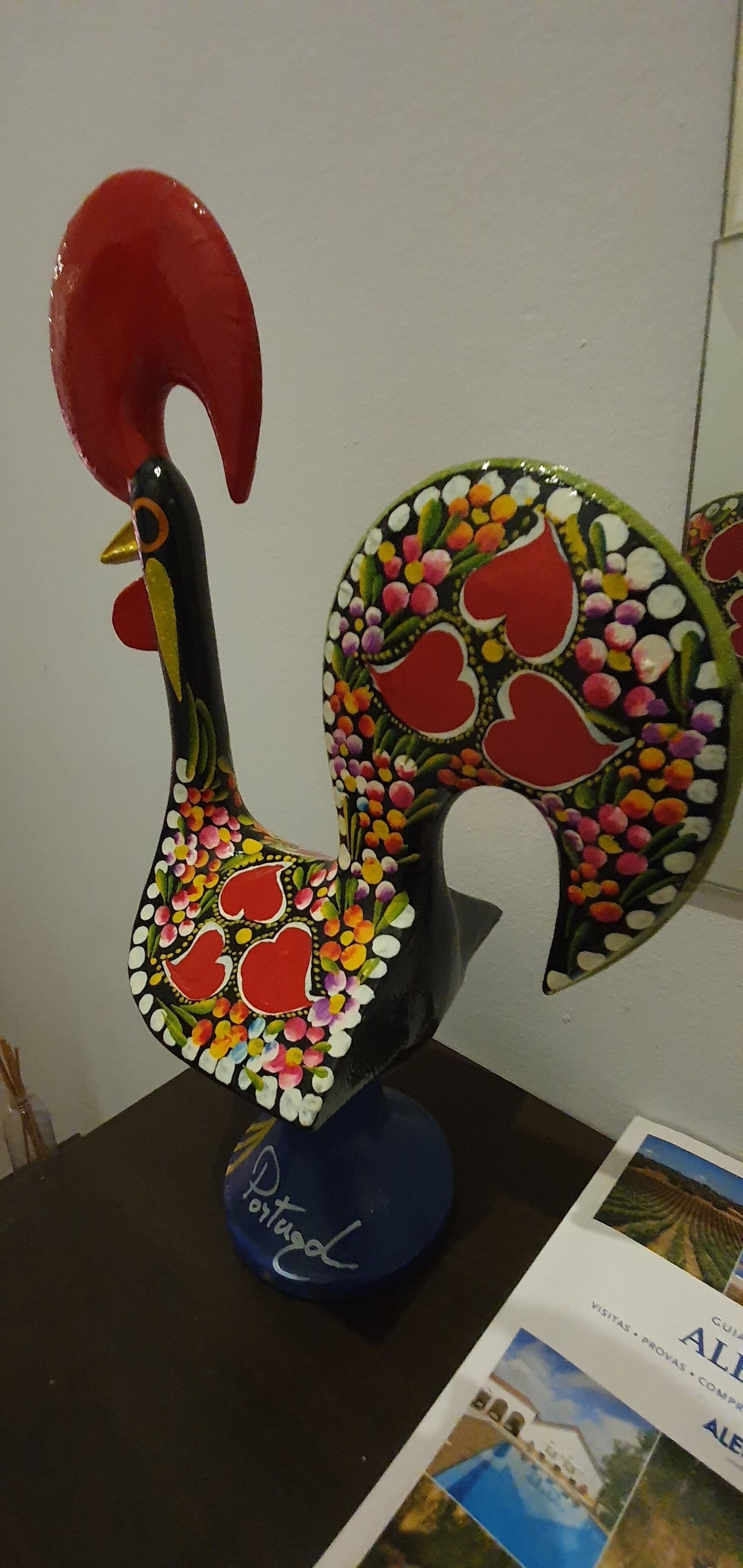 Eine dekorative Hahneskulptur mit blauem Sockel, platziert auf einem Tisch.
