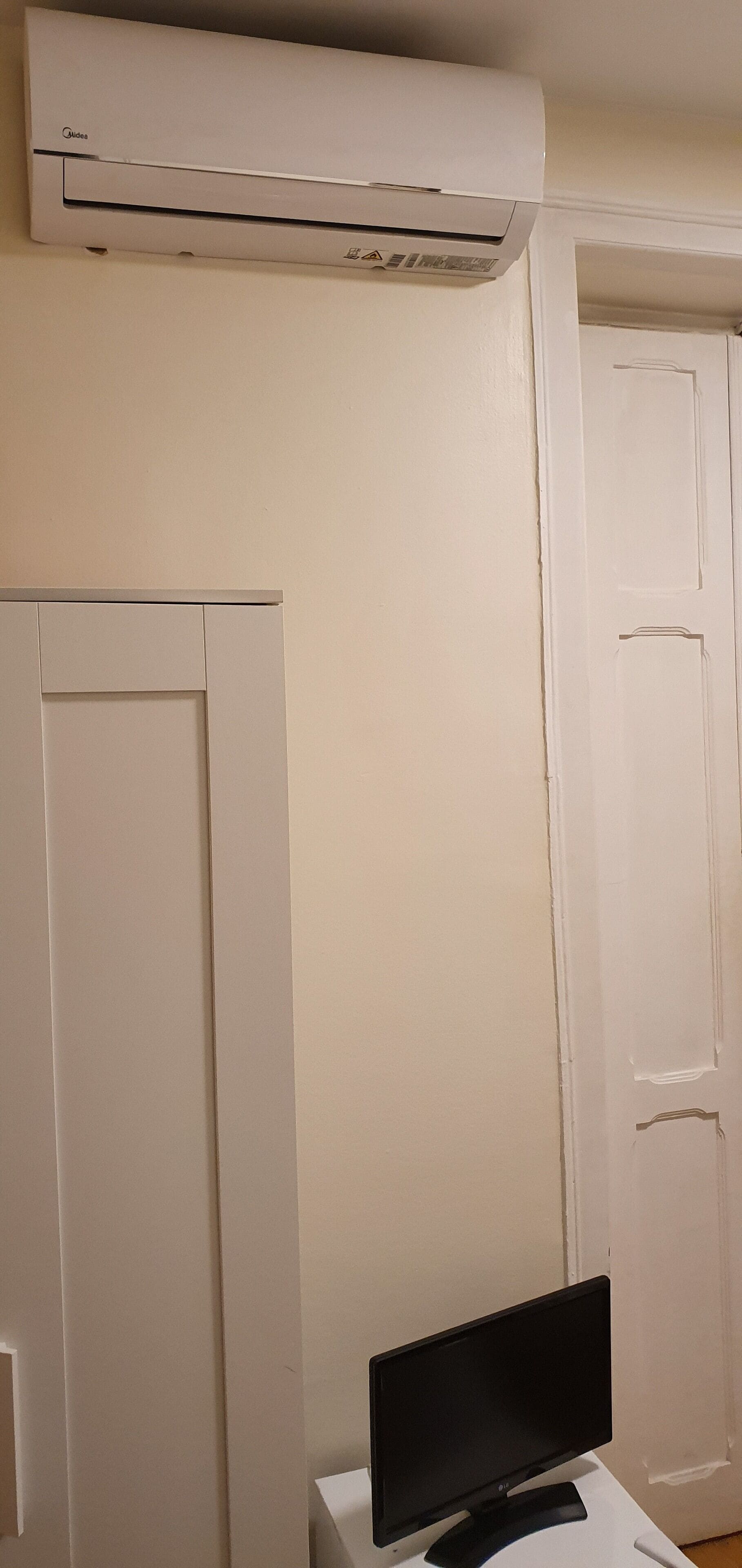Een kamer met een witte muur, een witte deur en een flatscreen televisie op een witte standaard.