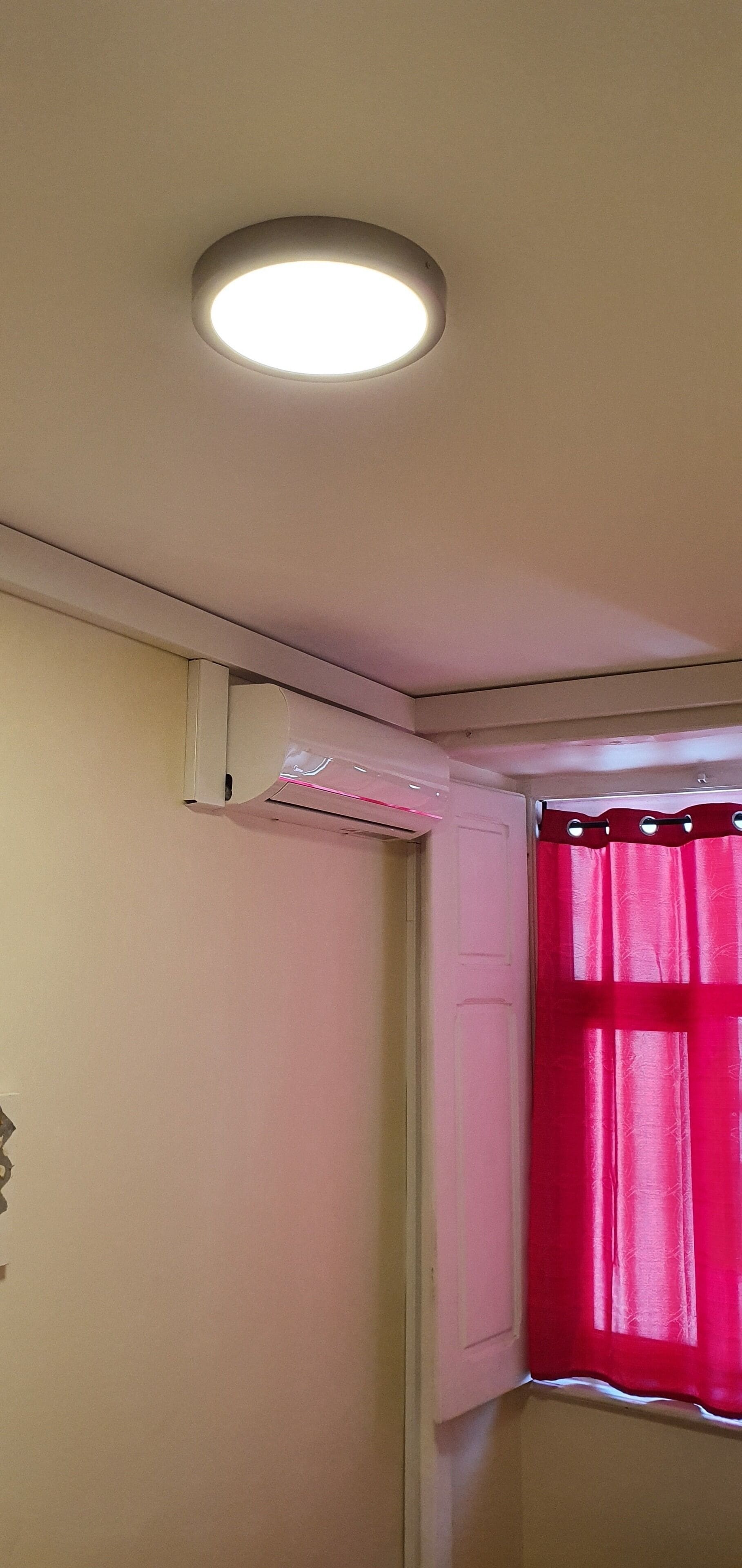 A room corner with a ceiling light, a white door, and a window with a red curtain.